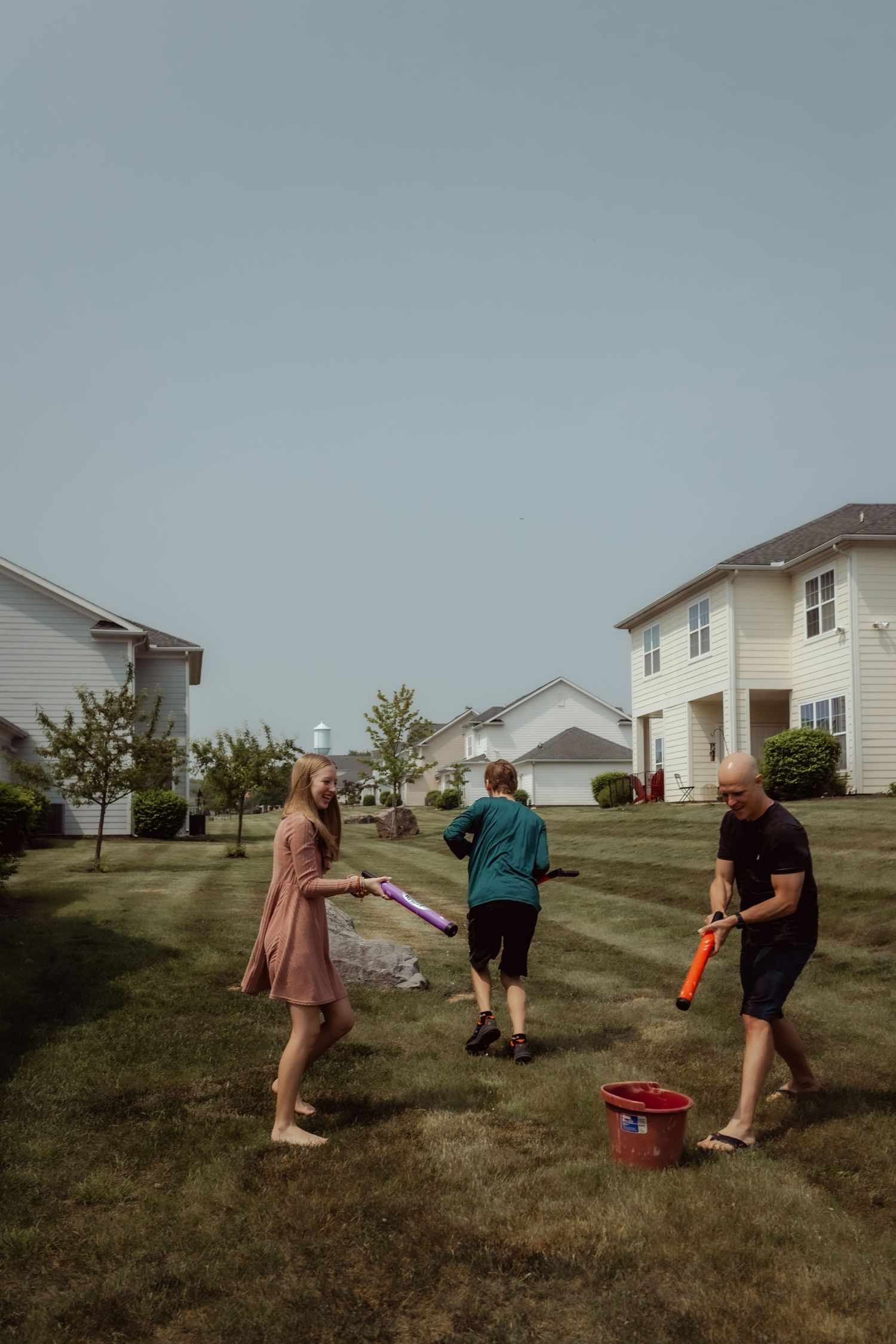 A group plays with water guns in a residential backyard on a summer day.