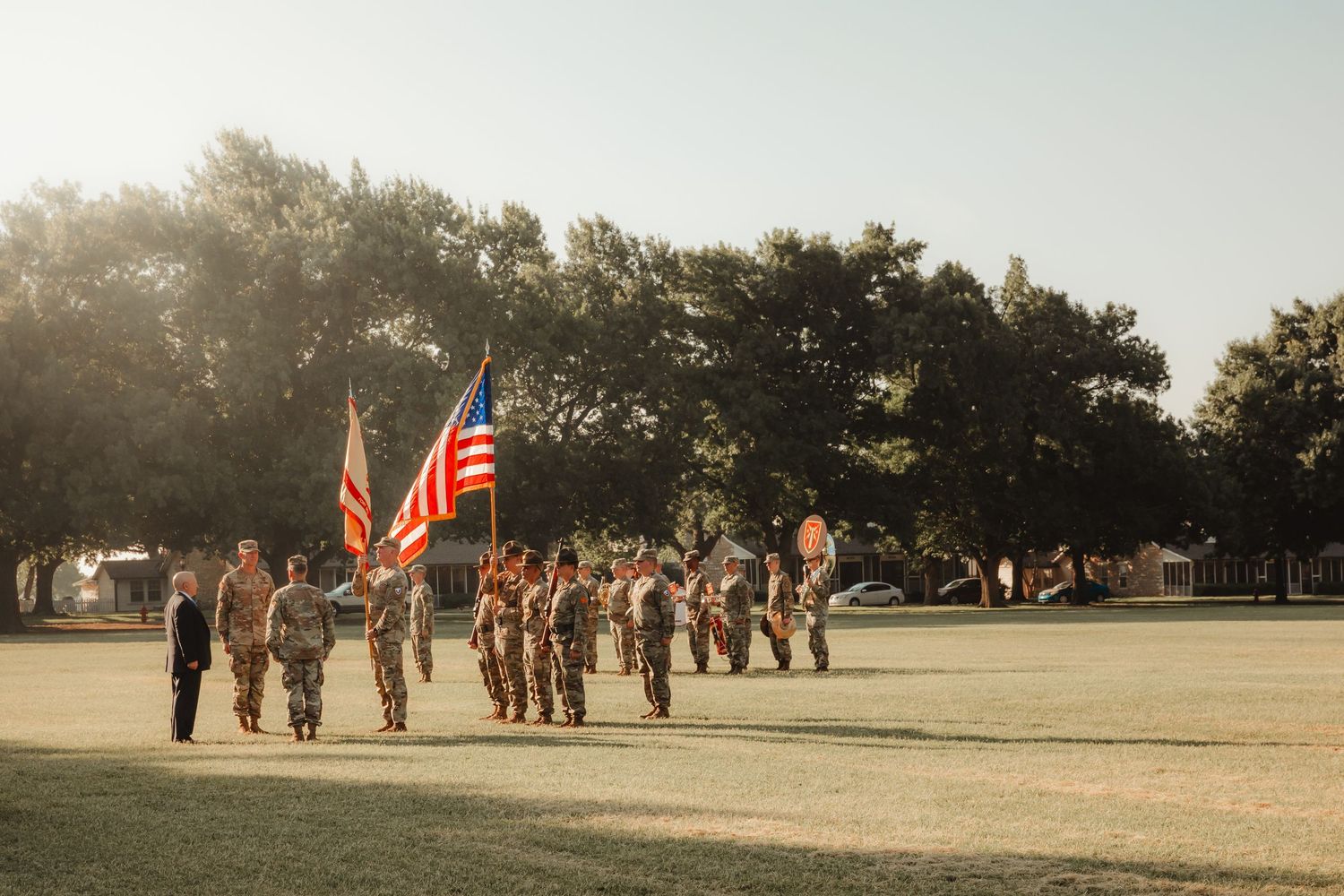 Military personnel stand in formation on a field with American flags during a morning ceremony.