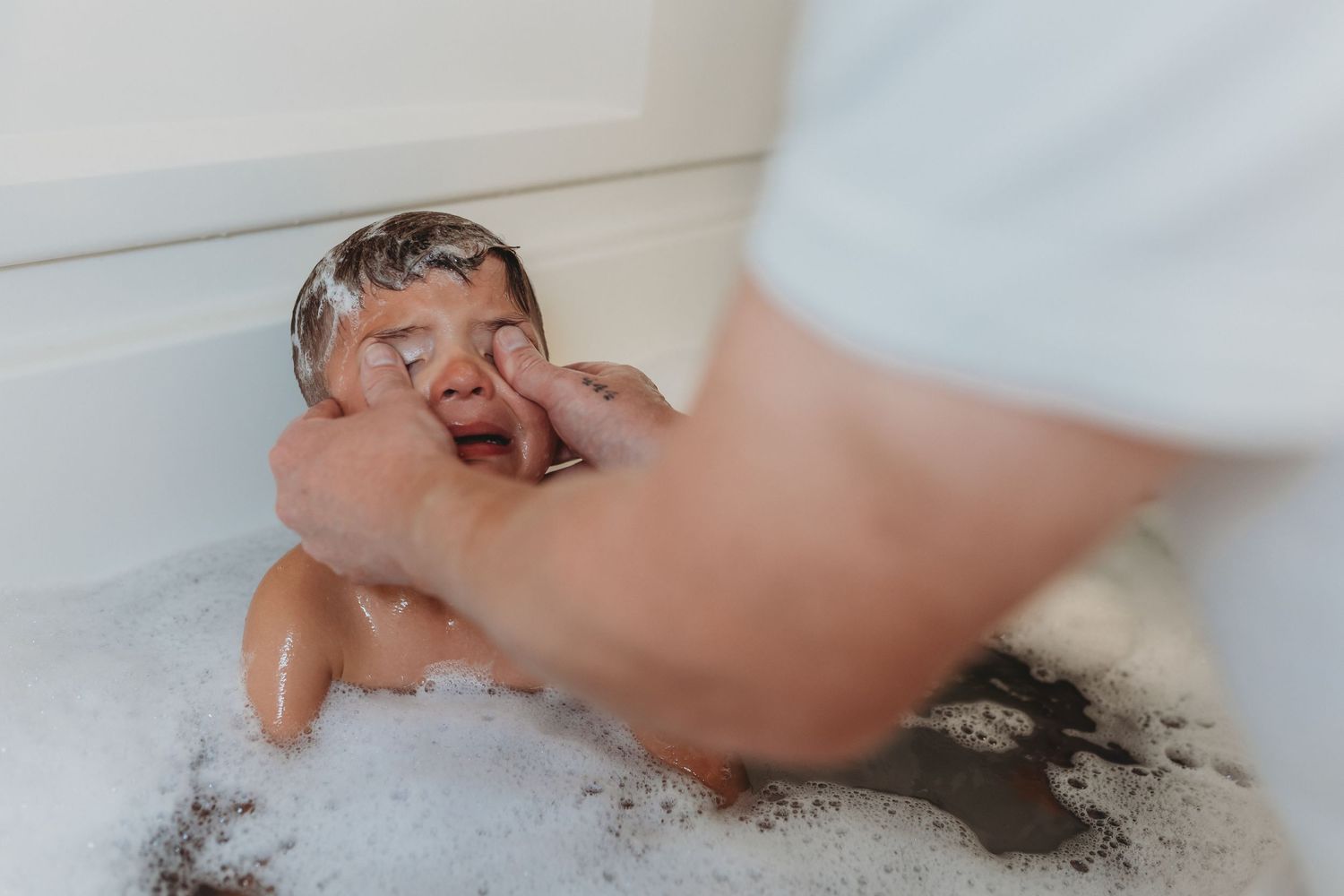 Closeup of hands playing in soapy bathwater creating bubbles.