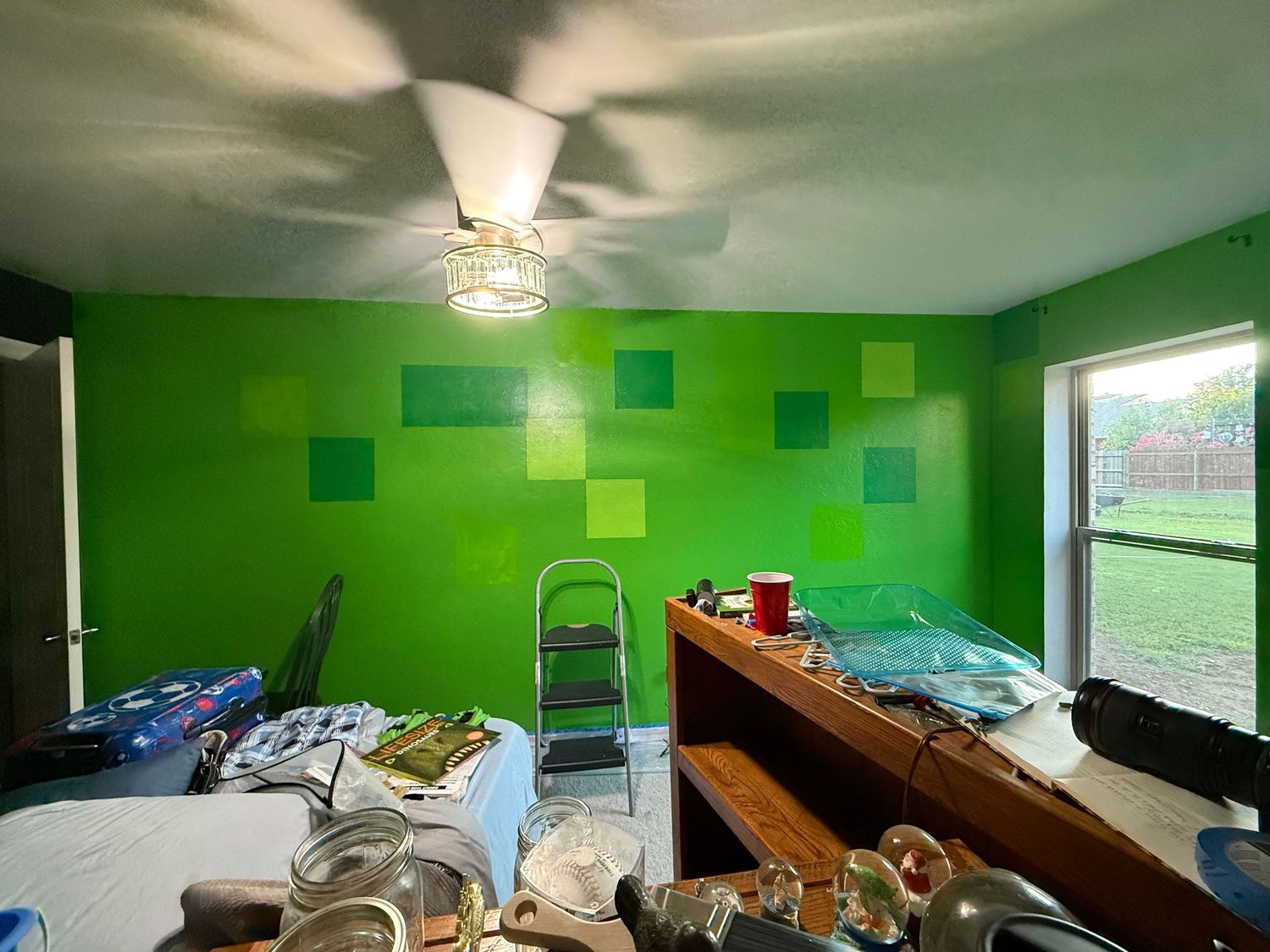 Green bedroom with painted geometric squares on wall shows renovation in progress with ladder and supplies scattered around. 
In-Home Photog