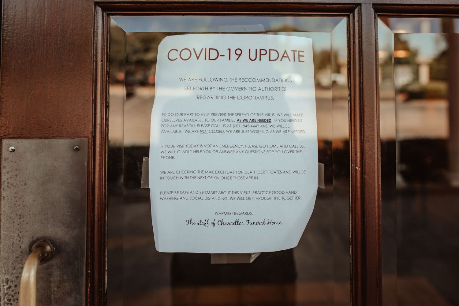A COVID-19 update notice posted on a glass door in a wooden frame providing service information.
