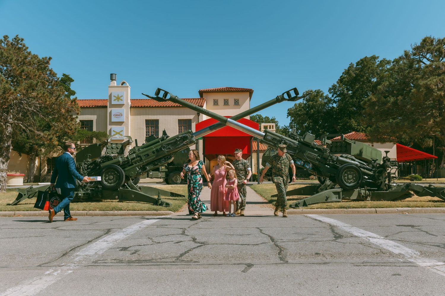 People gather in front of a military display with crossed artillery cannons outside a historic building on a sunny day.