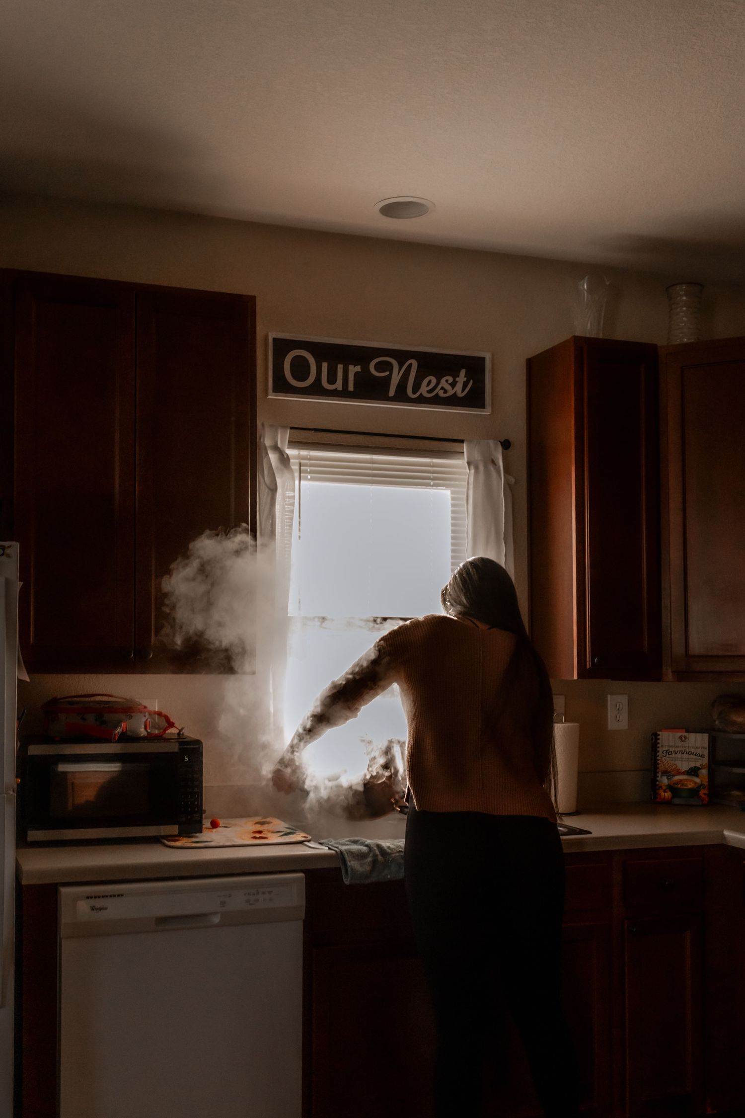 Steam rising in kitchen with 'Our Nest' sign above window.