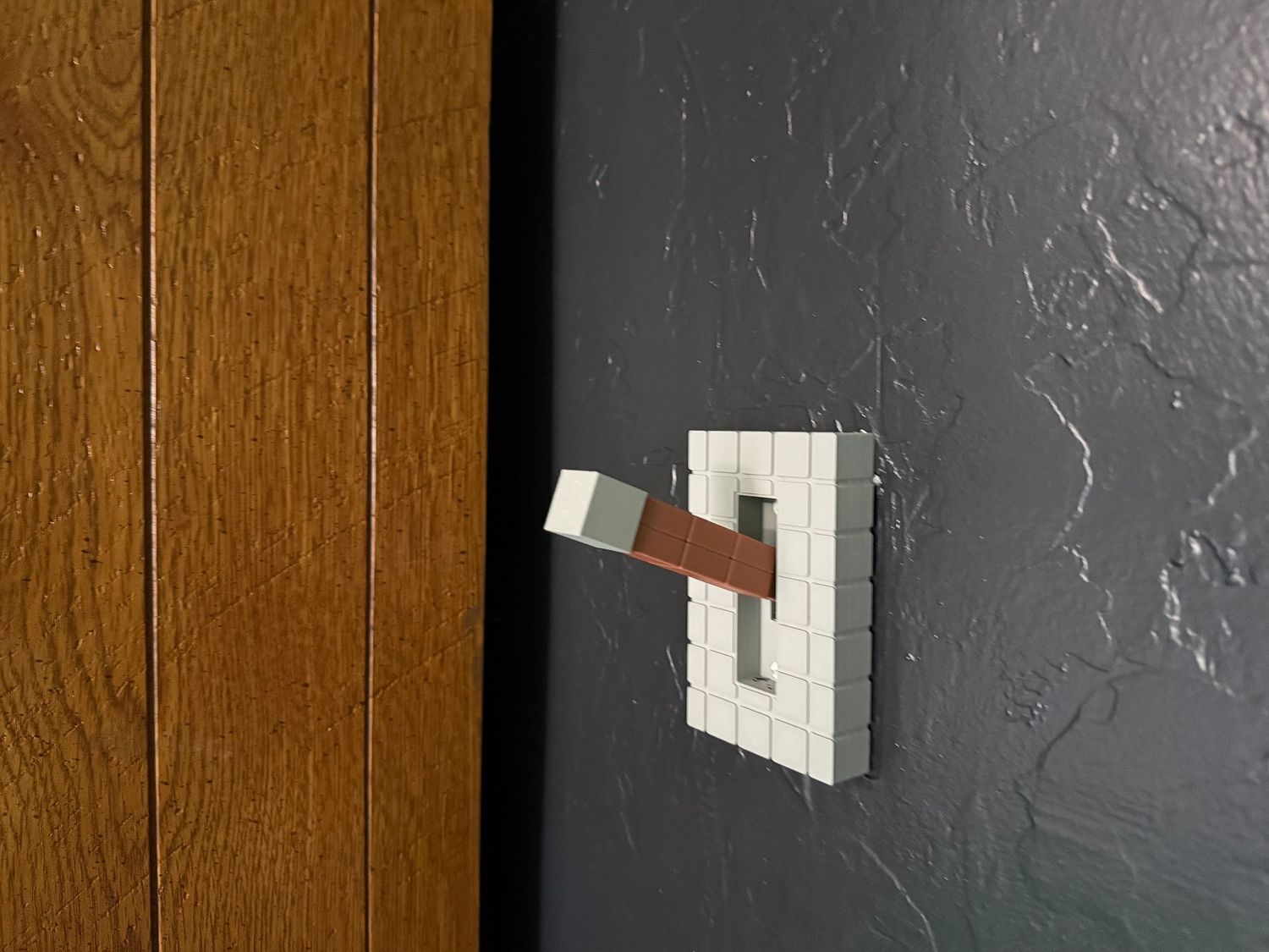 A white LED wall sconce fixture mounted on a dark textured wall next to wood paneling. In-Home Photography Liz Perez
