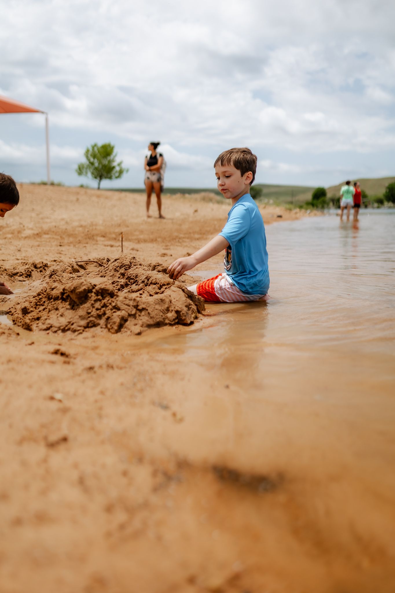 People sitting along the shoreline of a sandy beach on a cloudy day.