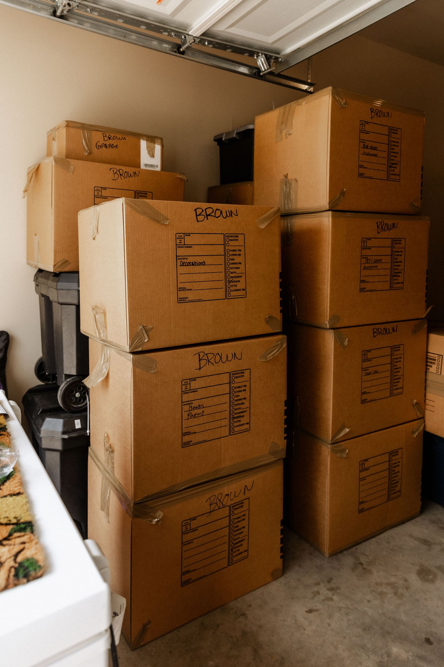 Stacked cardboard moving boxes labeled Brown fill a garage during a home relocation.