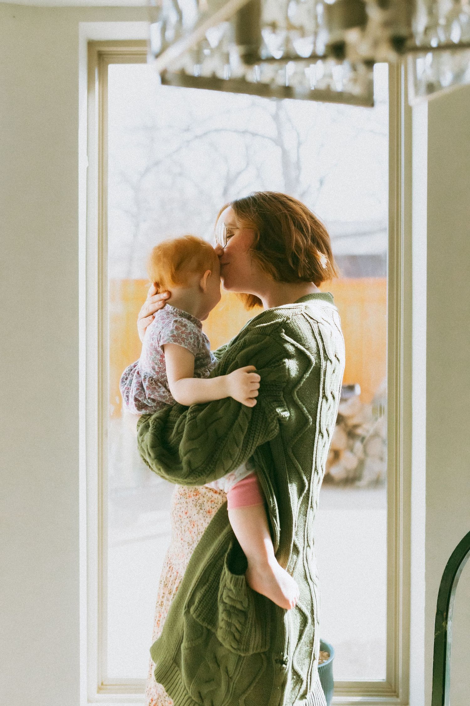 A couple embraces in a romantic dance pose near large windows with natural light streaming in.