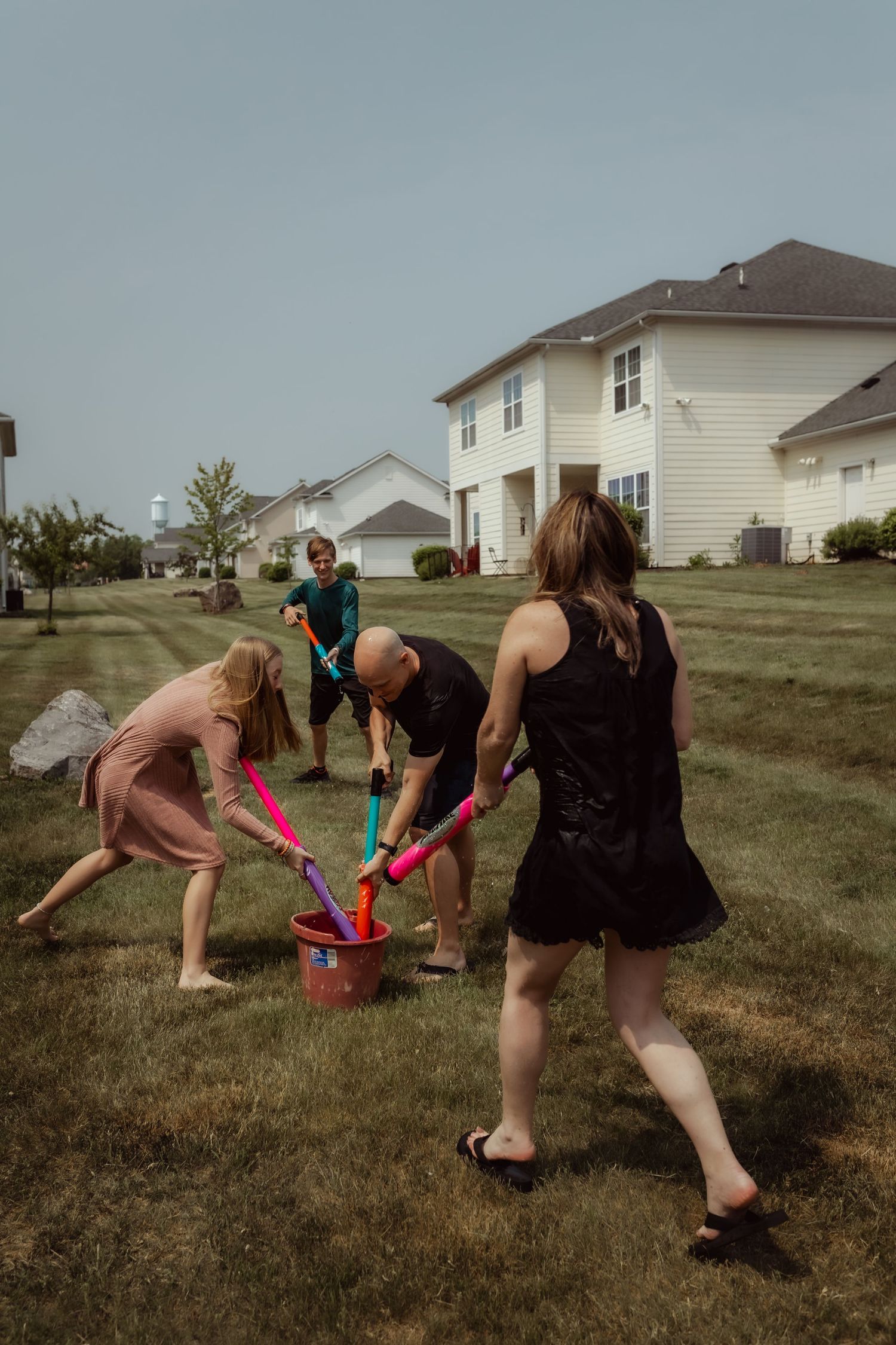 Friends gather around a bucket during an outdoor water fight game.