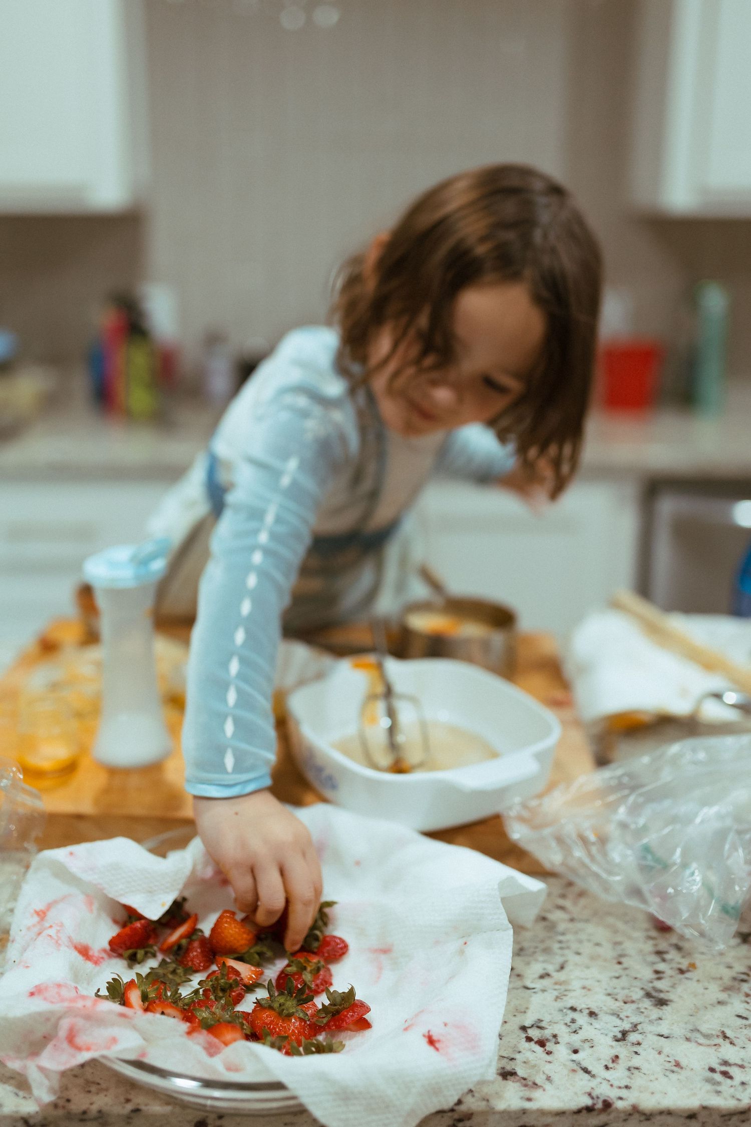 A person in a light blue sweater reaches across a messy kitchen counter covered in paper towels and ingredients. In-Home Photography Liz Per