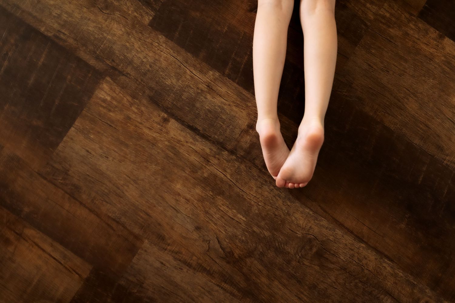 Bare child feet on dark brown hardwood floor, top view.
