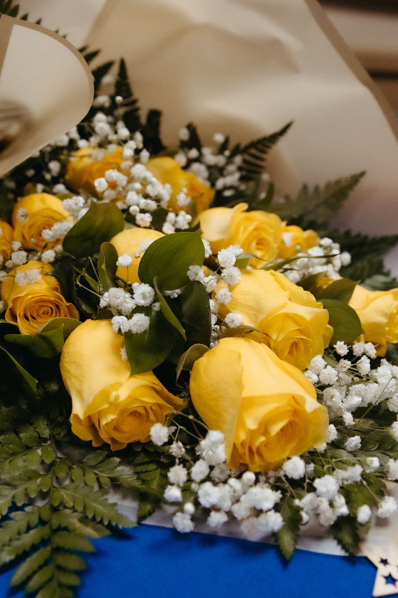 Yellow roses arranged with baby's breath and greenery against a blue background in an elegant floral display.