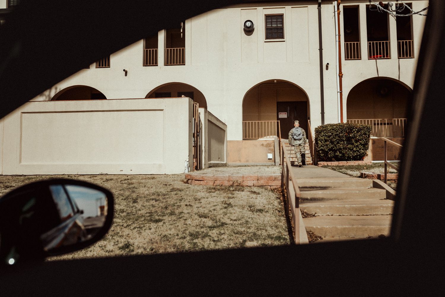 View through car side mirror shows white stucco building with arched architectural details and stone walkway.