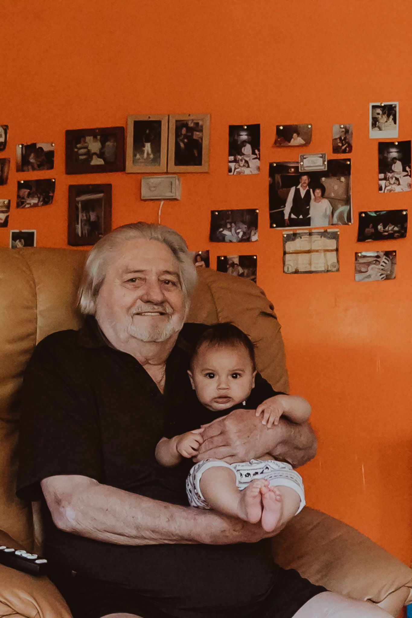 A candid moment in a room with orange walls and many family photos displayed.