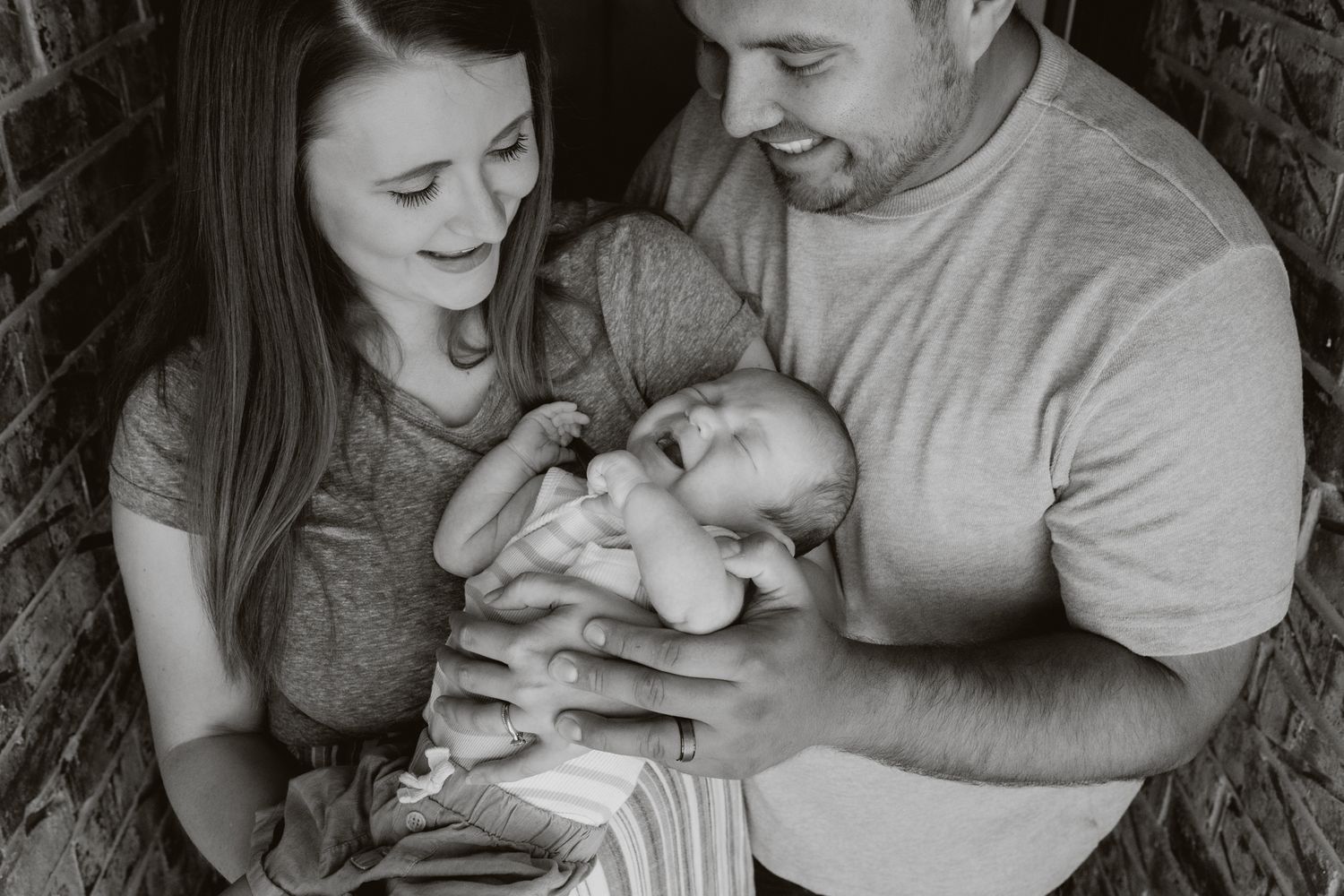 Black and white photo series showing tender moments between parents and their newborn baby against a dark background.