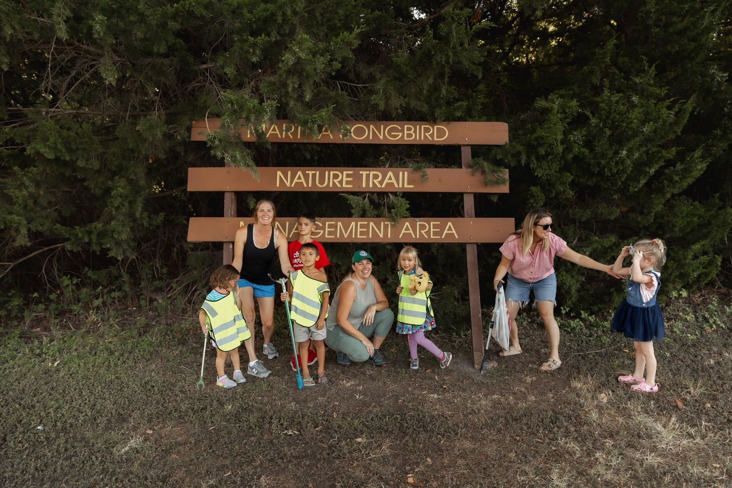 A wooden nature trail sign with a group standing beneath it at the entrance to a hiking area.