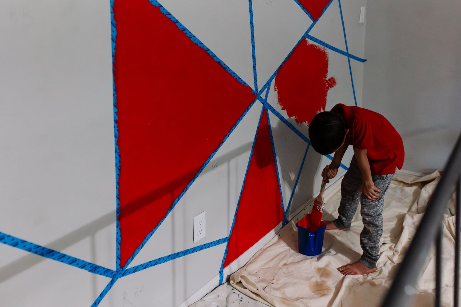 A series of red and white geometric shapes painted on a wall create an abstract architectural pattern.