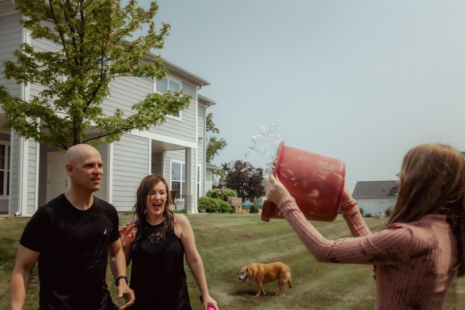 People splashing water from buckets during an outdoor water fight with a dog watching.