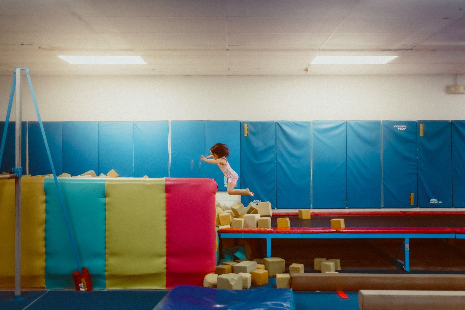 Young gymnast practicing on colorful equipment in a blue-walled gymnasium.