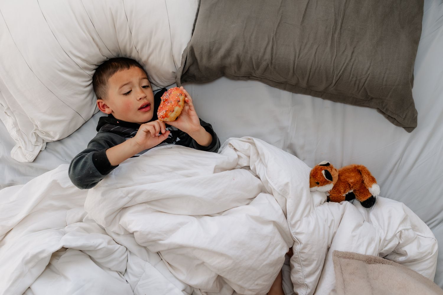 Person sleeping peacefully in comfortable white bedding with cozy gray pillows.