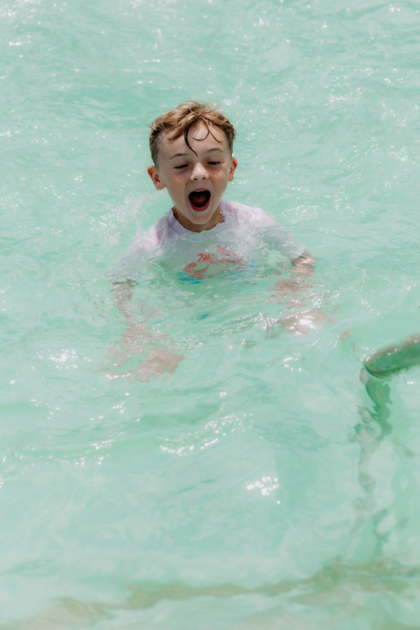 Young swimmer enjoying turquoise water with excited expression.