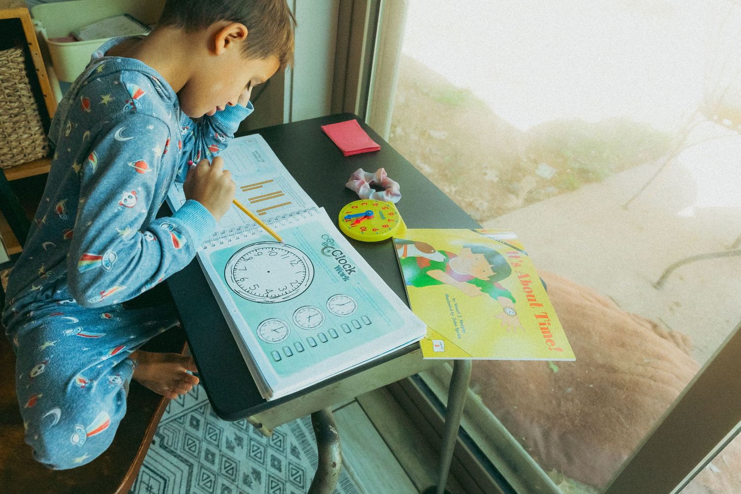 A student wearing a blue smock sits at a table working on drawing or coloring activities in an educational setting.