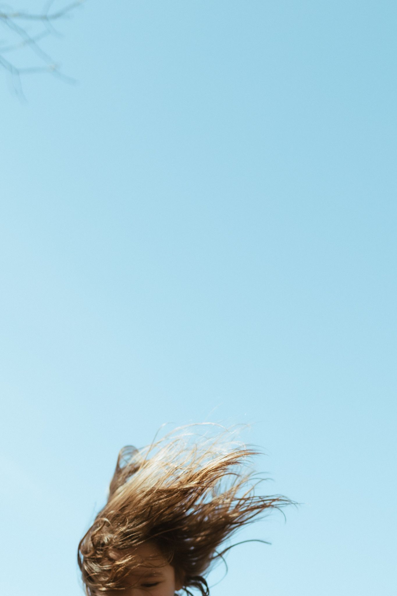 Person with long hair blowing wildly in the wind against a clear blue sky.
