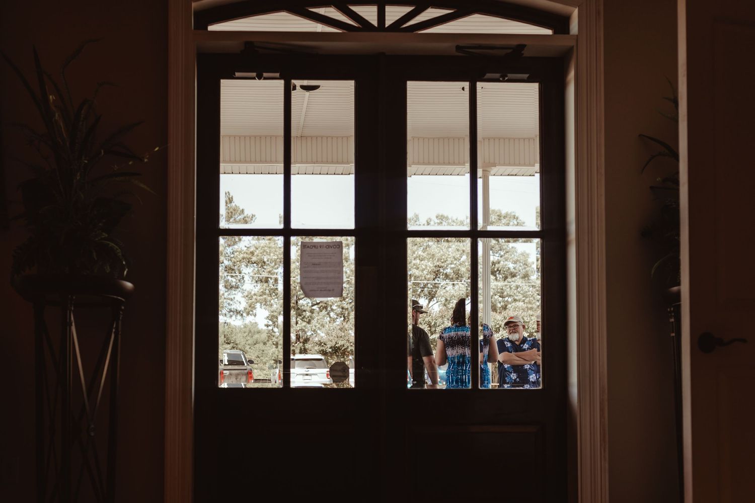A silhouetted view through ornate doors showing people gathered outside in daylight.
