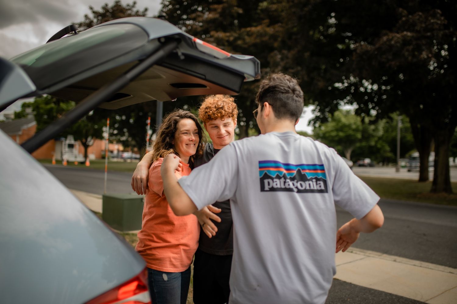 People in casual attire gathered around a vehicle in a suburban setting.