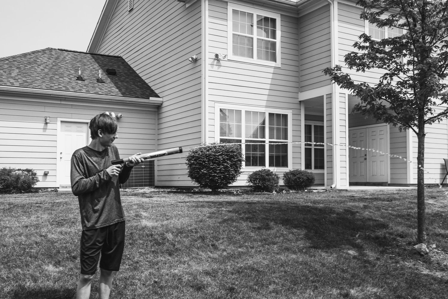 Person in dark clothing aiming a water gun in front of a suburban house.