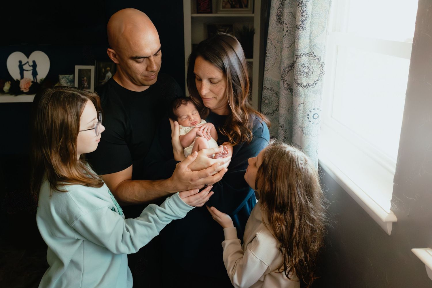 Family members gather around to admire a newborn baby in a cozy home setting.