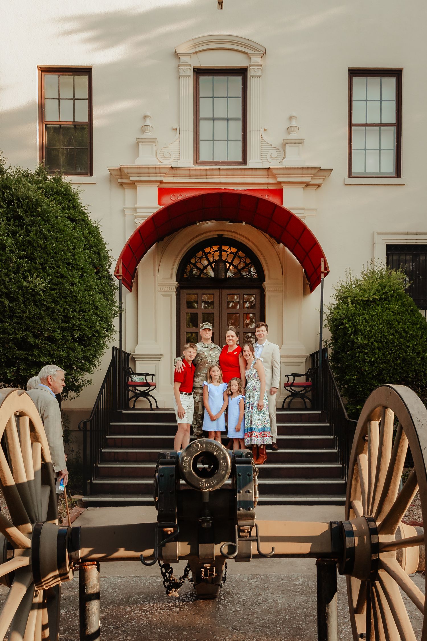 Historic white building entrance with red awning and antique cannon and wagon wheels in foreground.