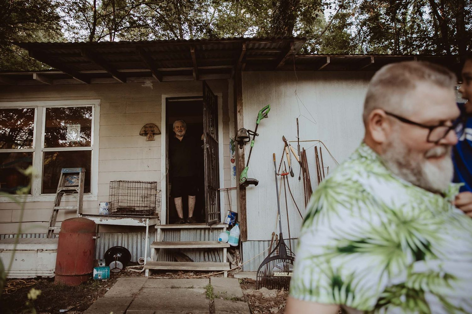 A view of a small white house with a front porch and garden tools leaning against the wall.