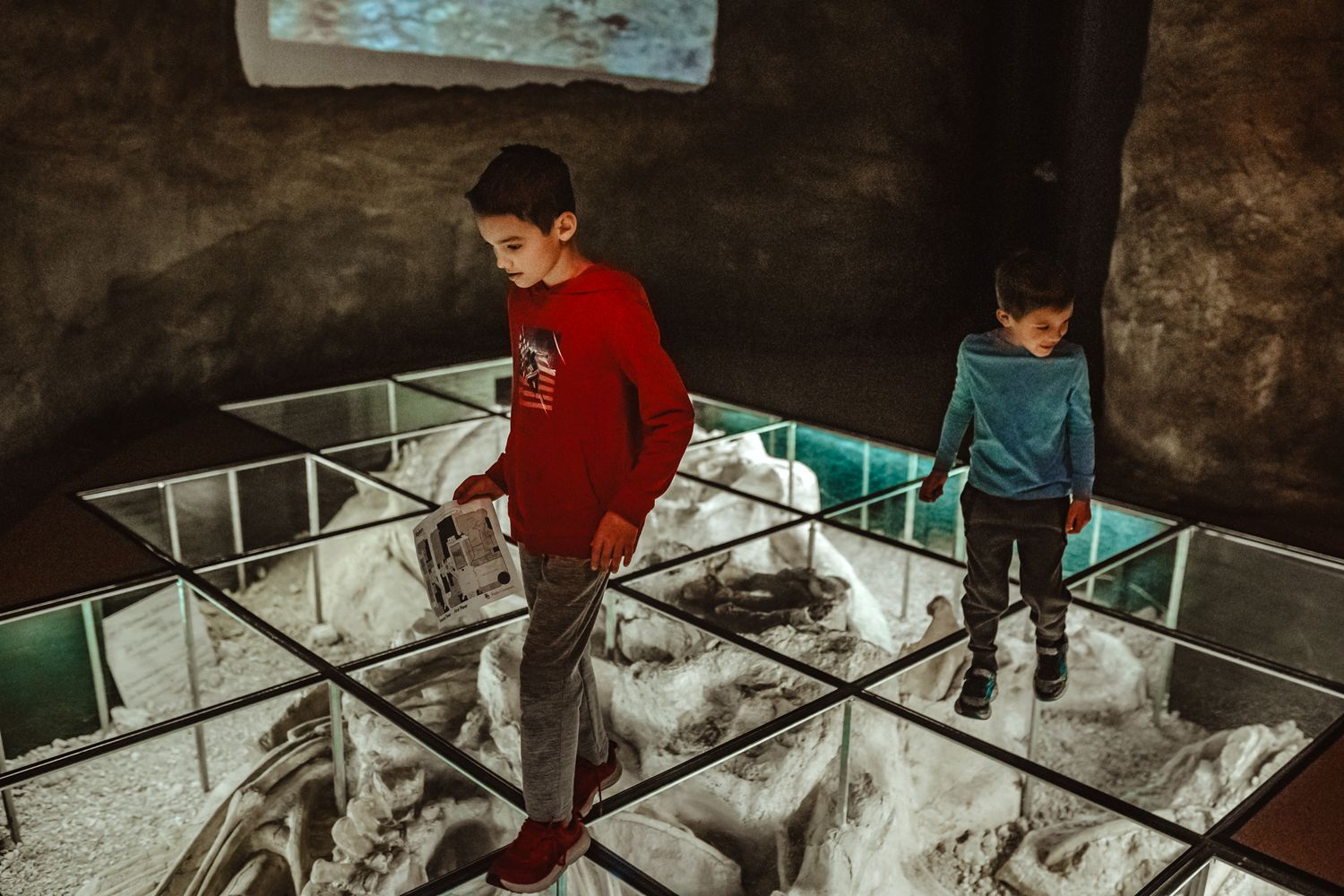 Child in a red sweater studies artifacts displayed behind glass cases at a museum exhibit.