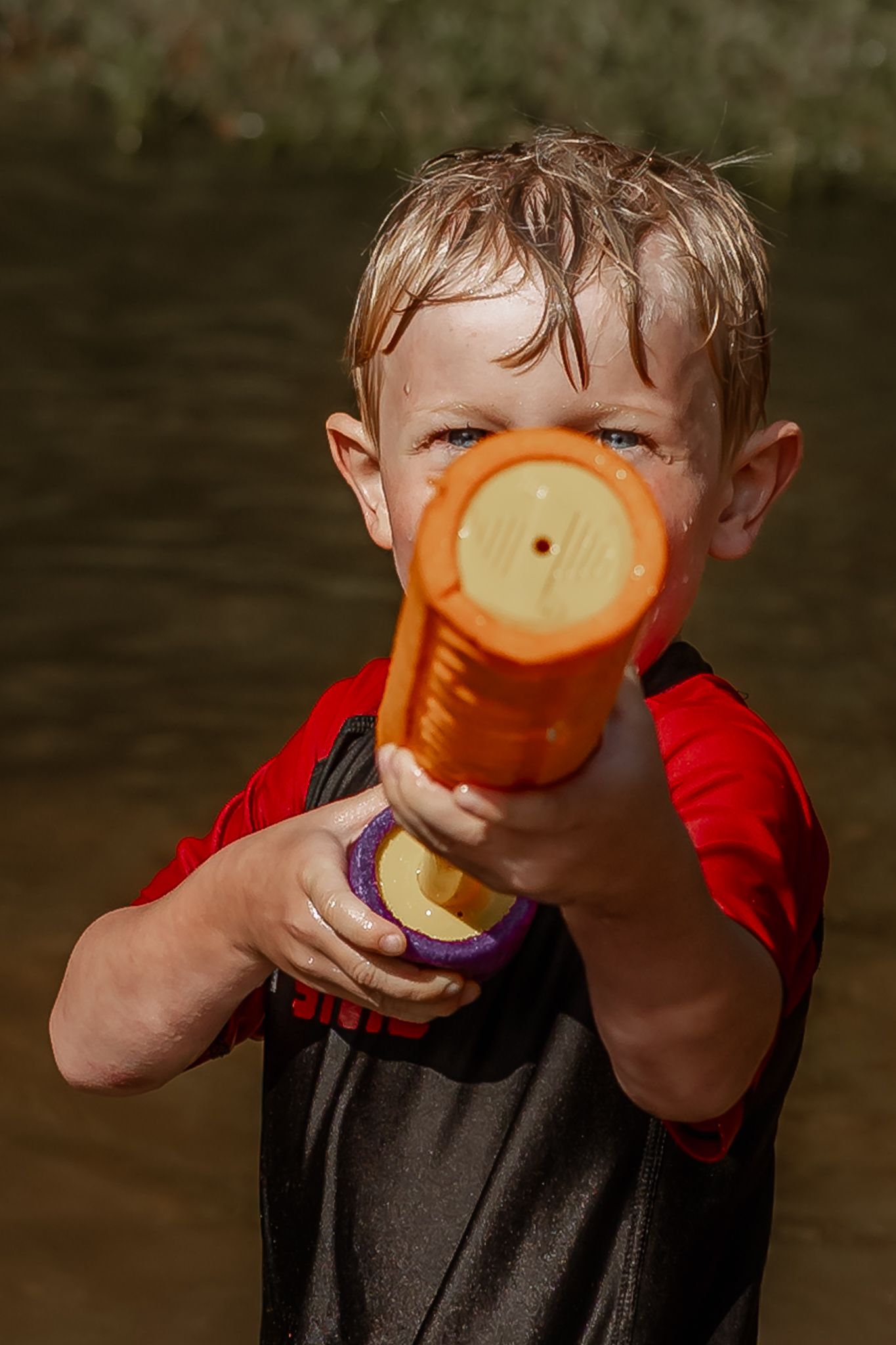 Child holding orange water gun against nature background.