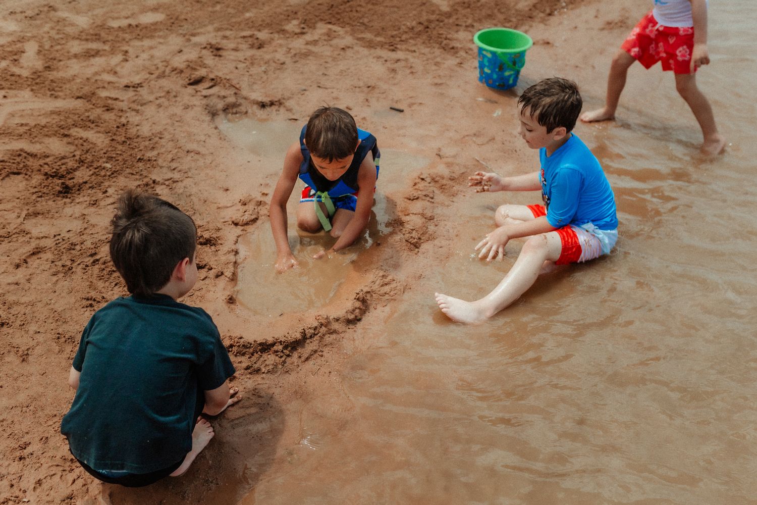 Children playing in sand and shallow water at lake edge.