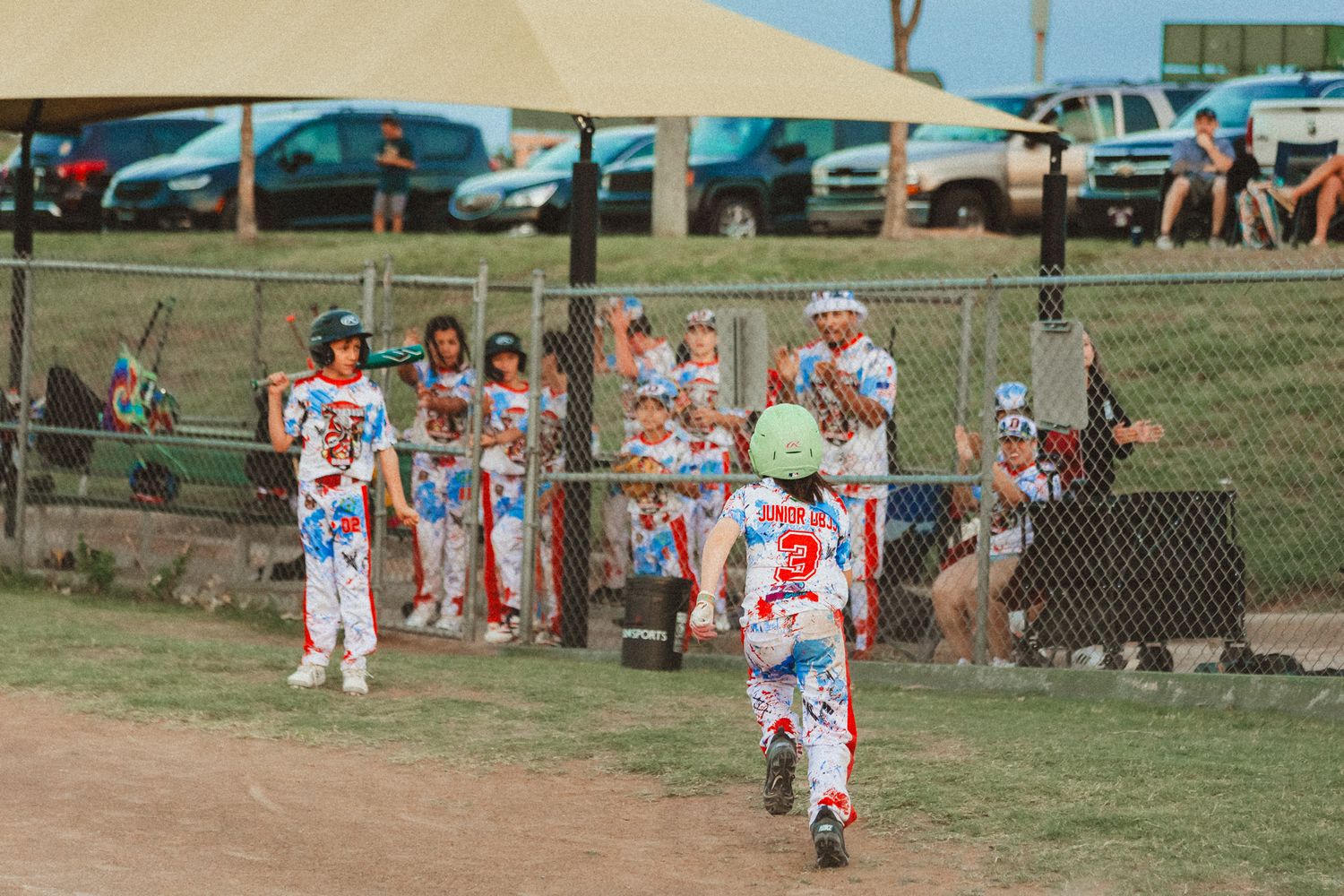 Young baseball players in colorful uniforms playing a little league game on a dirt field with spectators watching.