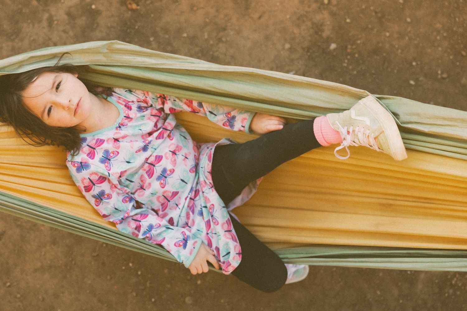 Person relaxing in floral dress on striped hammock on sunny day.