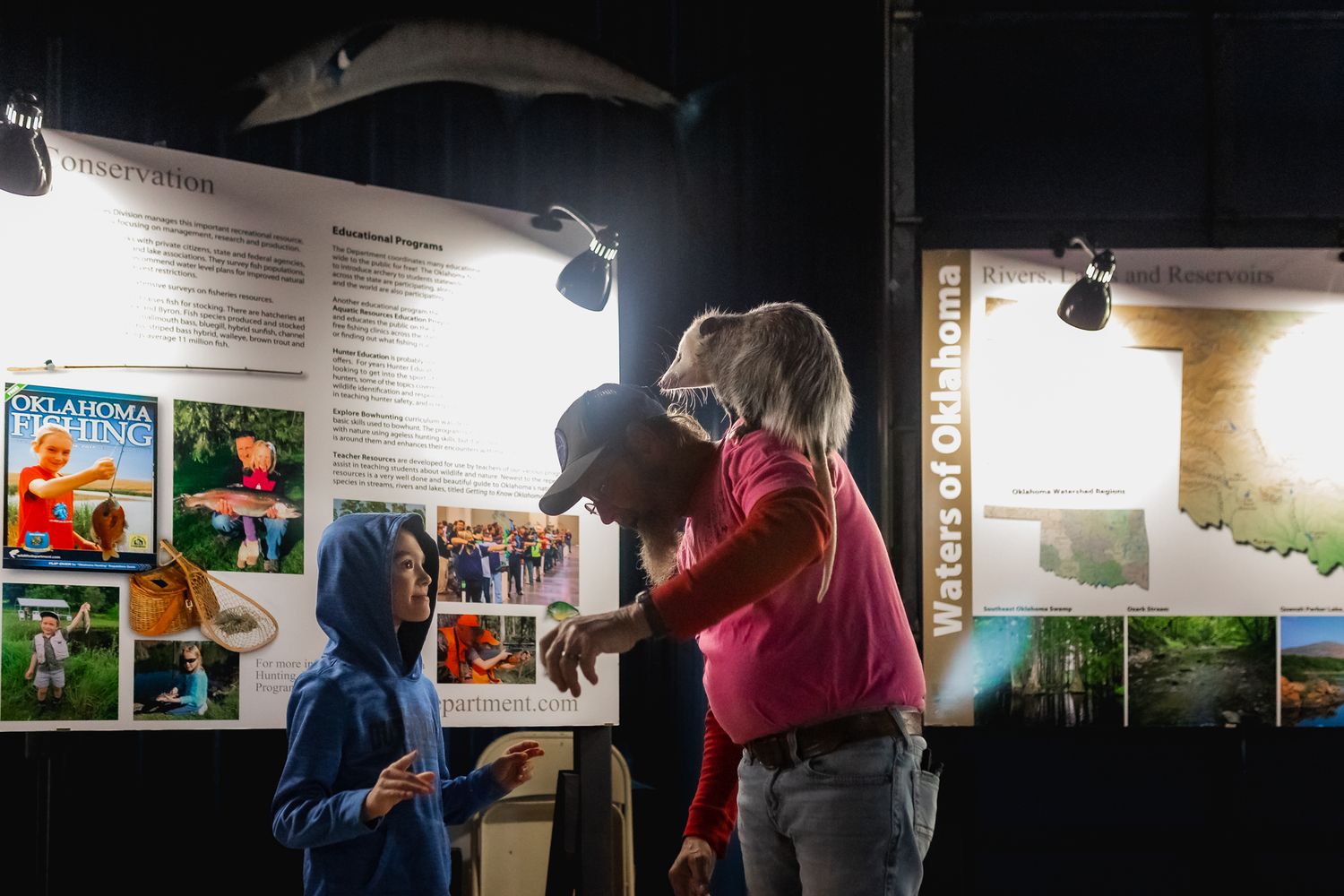 Exhibition gallery displays photos and artwork on walls under spotlights.