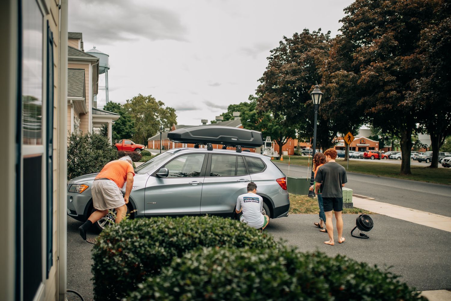 People loading luggage onto car roof rack on suburban street. In-Home Photography Liz Perez