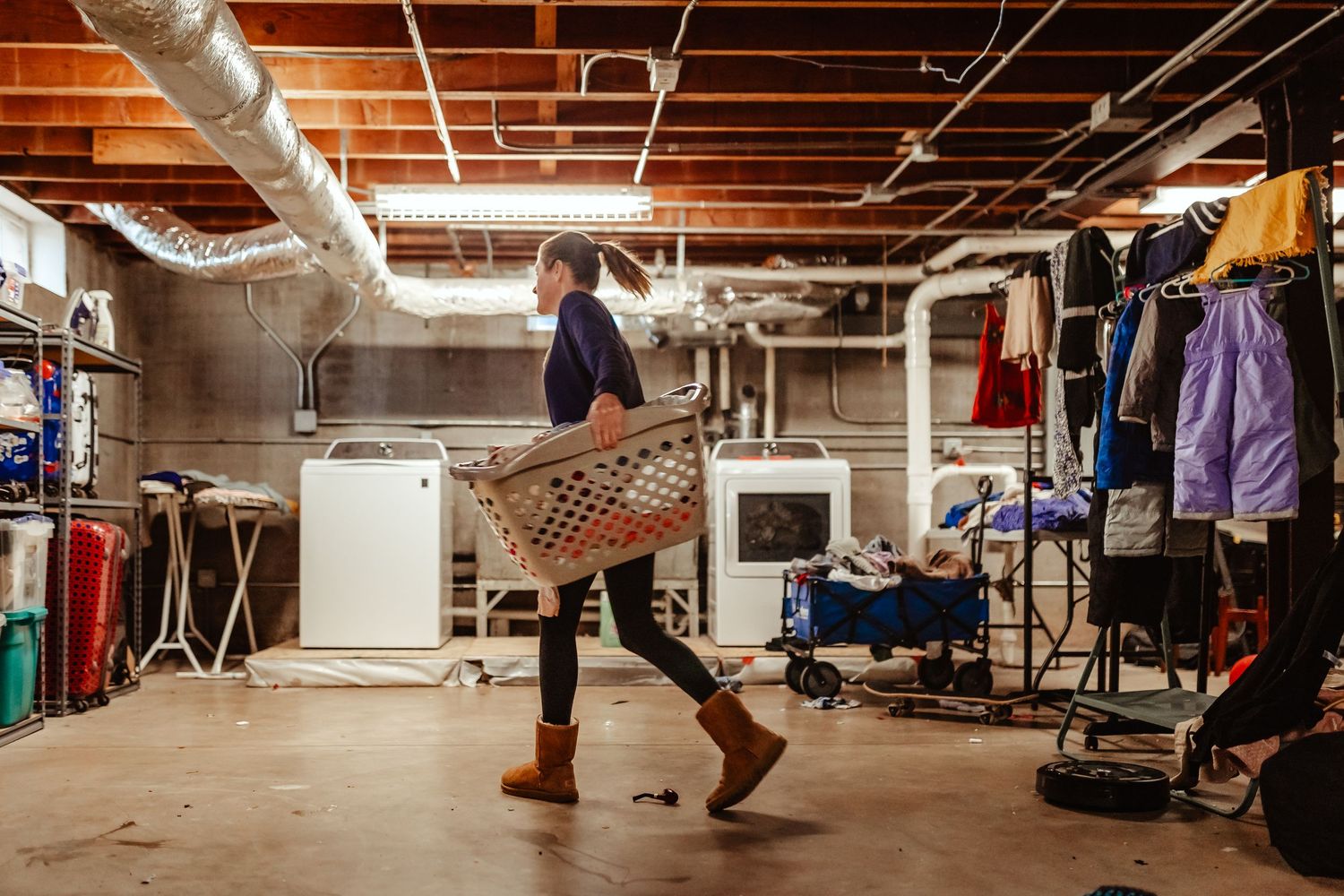 Woman carrying laundry basket in unfinished basement in Fort Sill, OK housing using documentary family photography with Liz Perez.