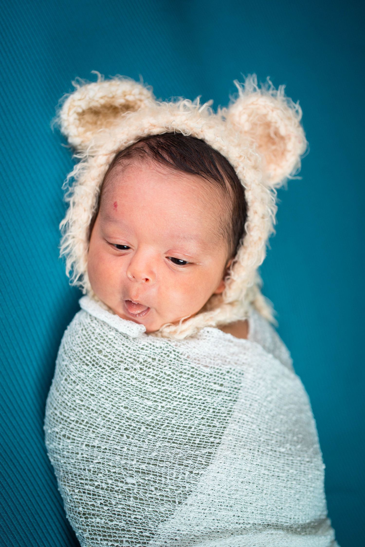 Warrensburg newborn session where baby is wearing a teddy bear hat and sticking his tongue out
