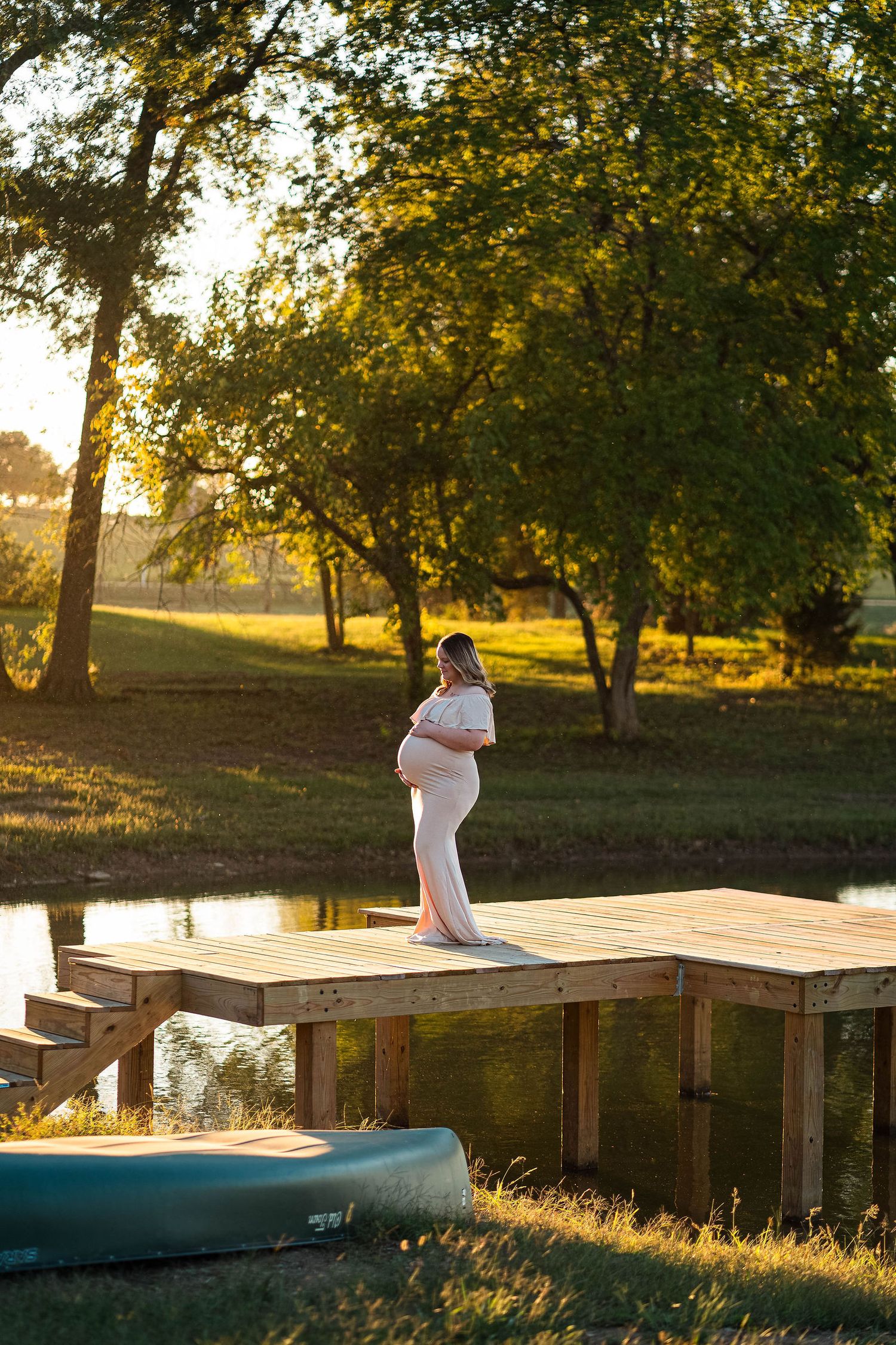 A mom is on a dock over a lake during her maternity session in Lee's summit