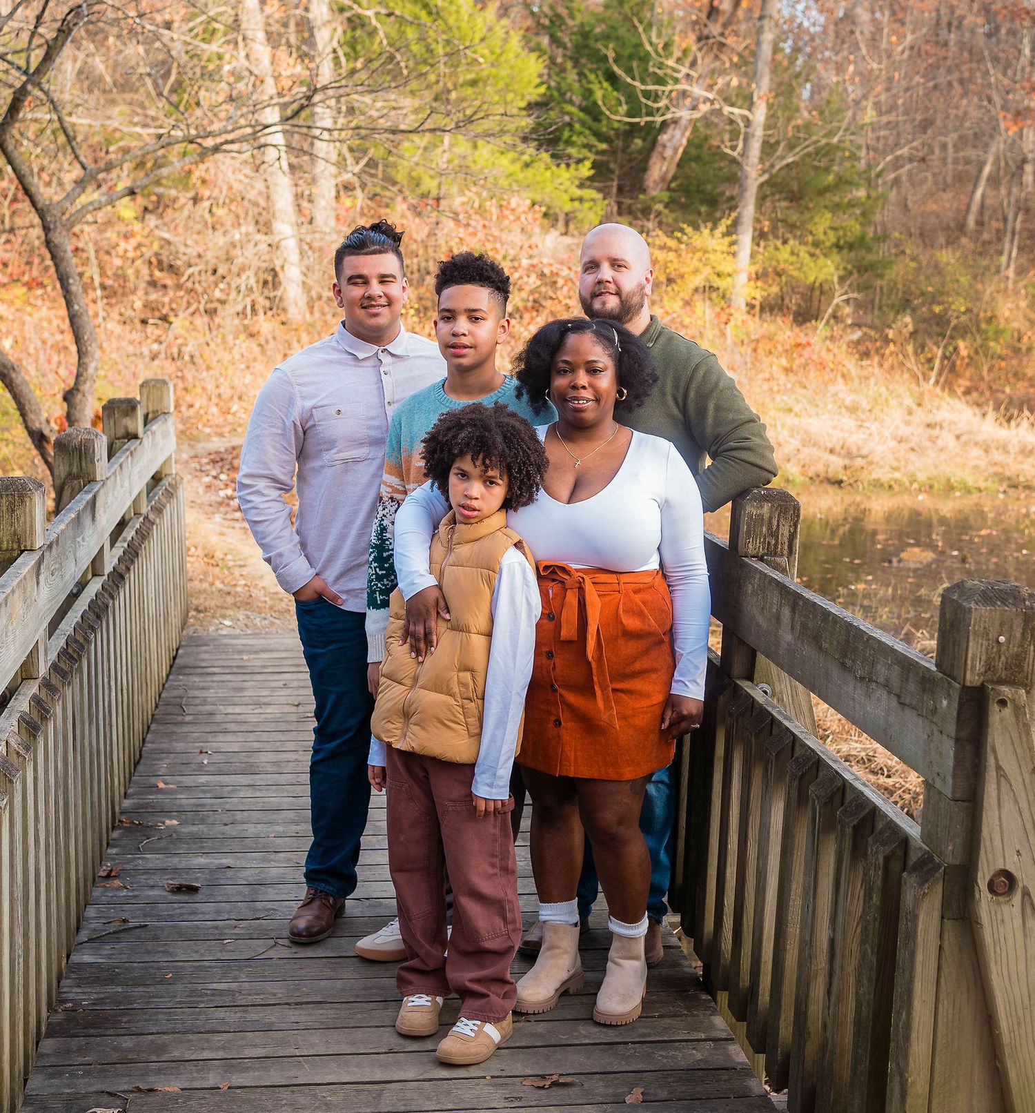 A family smiles at the camera during their family photo session by the lake in Knob Noster State Park
