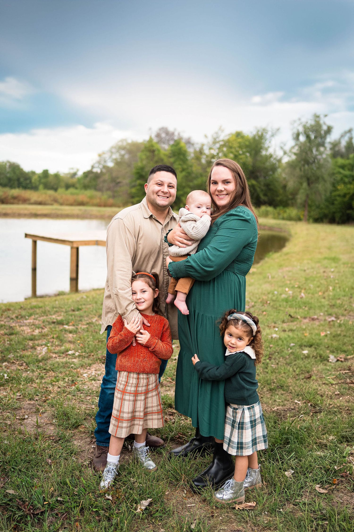 A family cuddles close and smiles at the camera by a pond at their family photography session located in Knob Noster