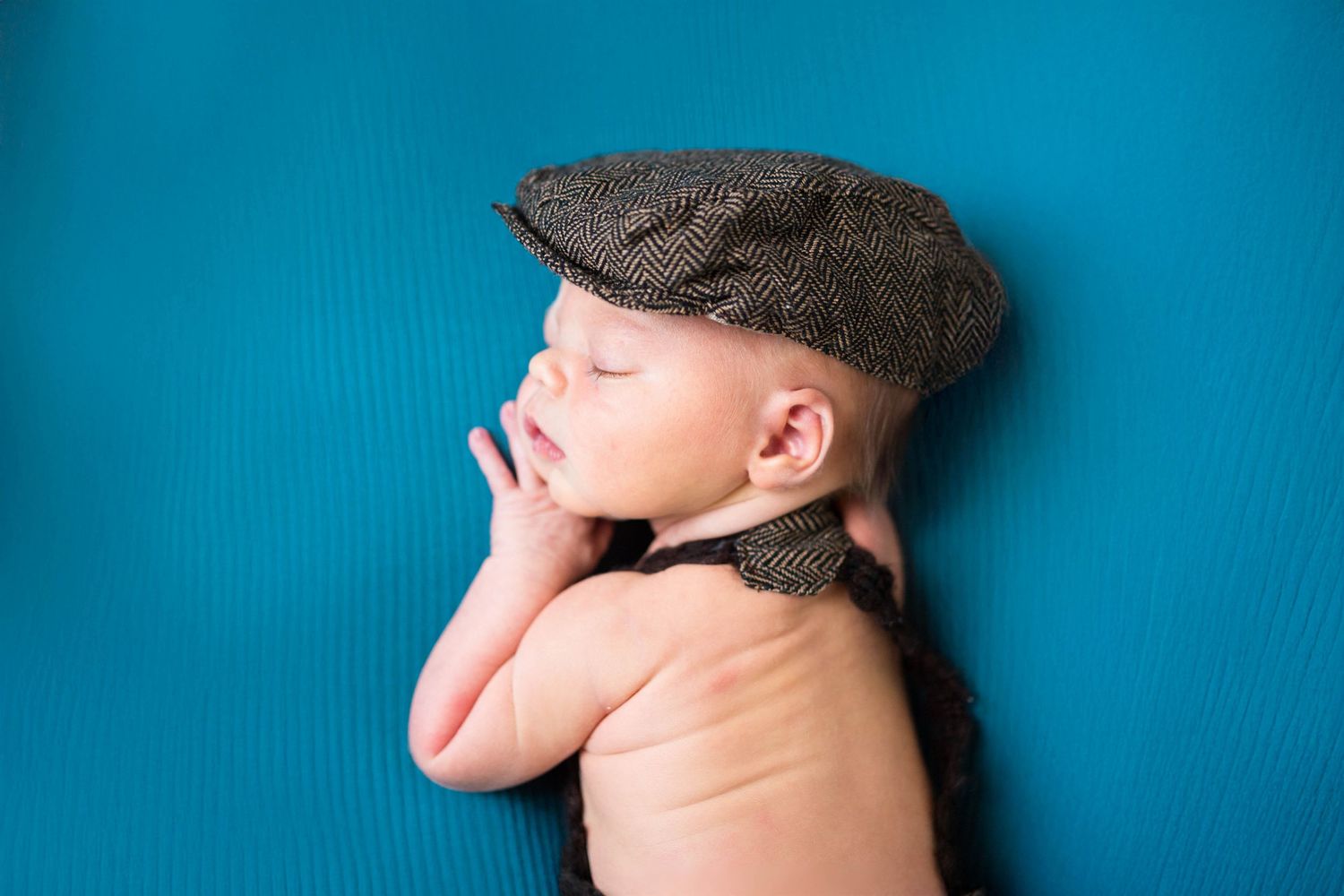 a baby cuddles up in a blanket and hat during his newborn session in-studio in Warrensburg