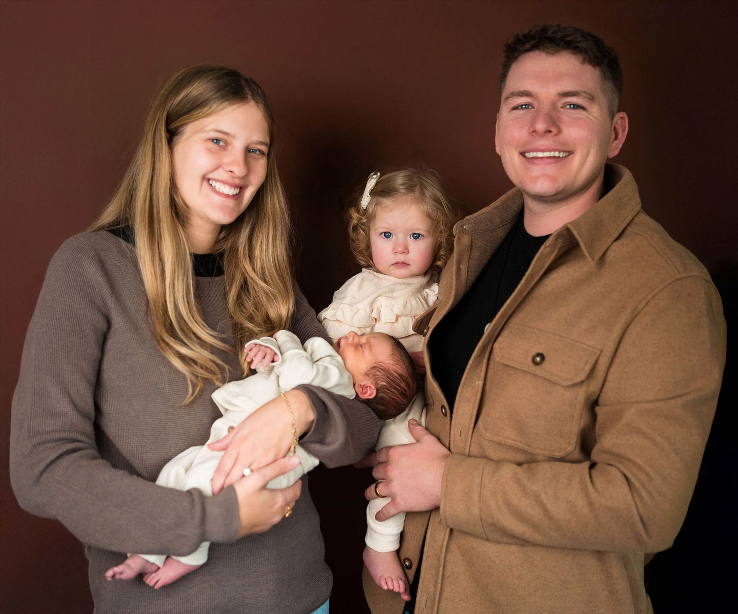 A family smiles at the camera during a newborn session for the baby in the photographers studio in Warrensburg