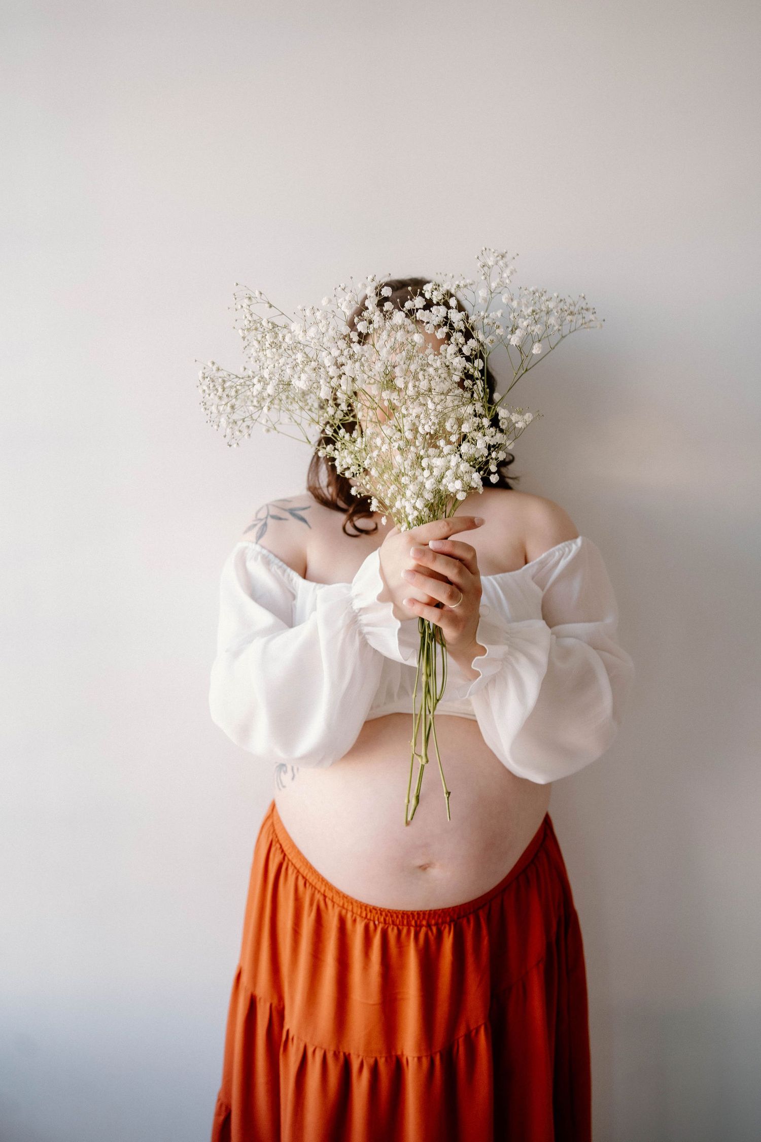 a pregnant mom holds flowers infront of her face during her in-studio session in Warrensburg, MO