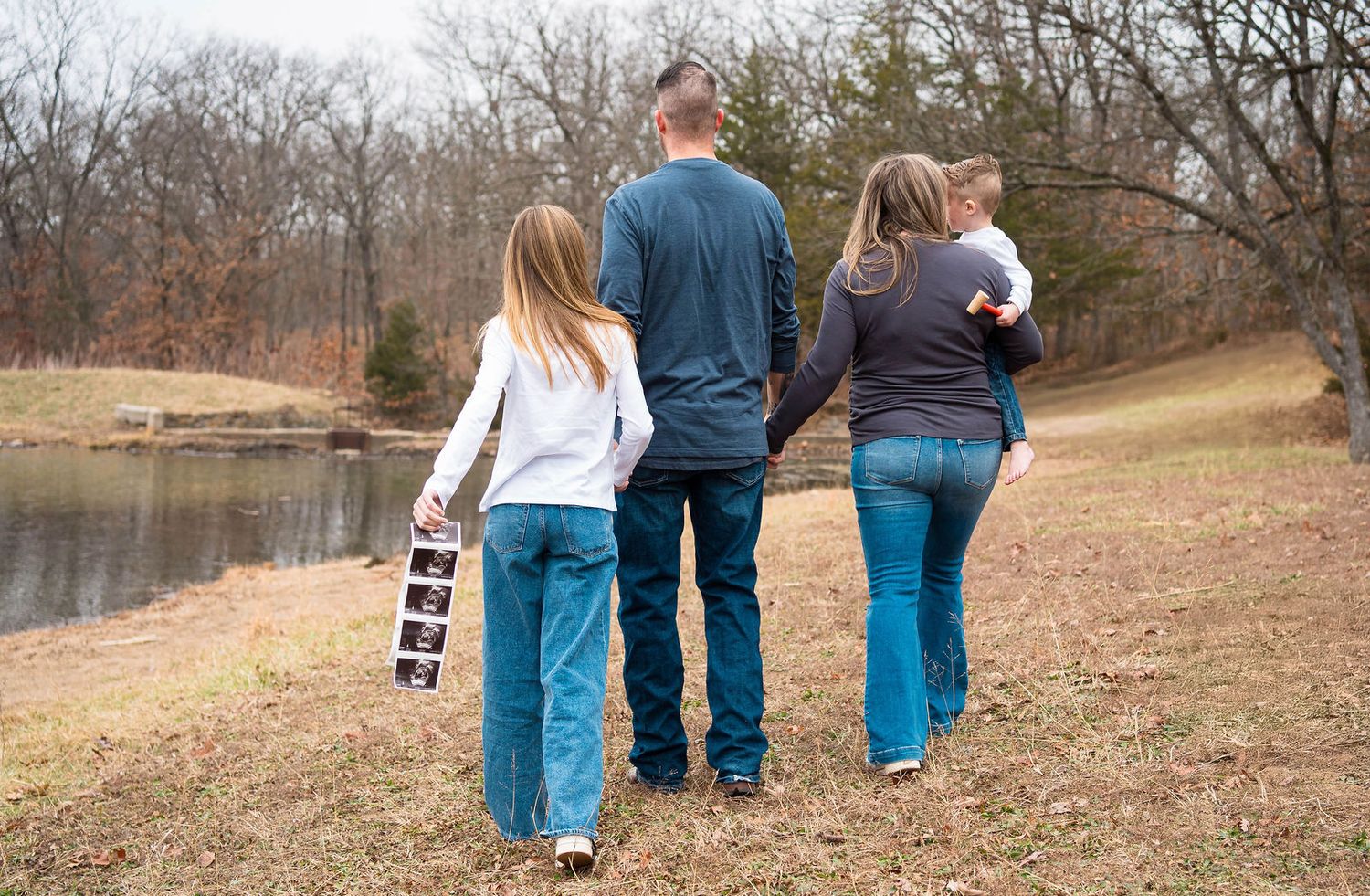 A family walks away from the camera announcing a pregnancy during a family and maternity session in Kansas City, MO