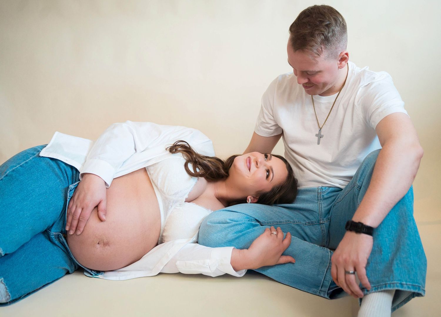 a  couple smile at each other while sitting on the ground during their instudio maternity photography session located in Warrensburg