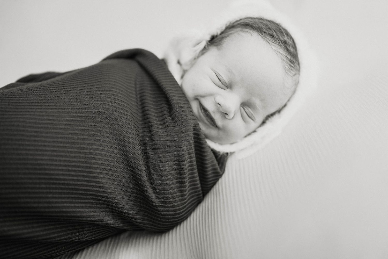 a baby is all snuggled up and smiling during his session in Knob Noster